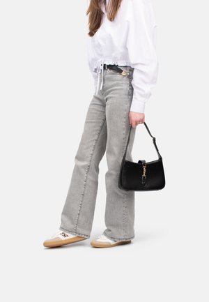 Jeans svasati grigio chiaro, camicia bianca a maniche corte e bottoni, borsa nera con accessori dorati e sneakers bianche con suole beige.