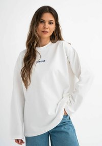 Witte sweatshirt met een ronde halslijn en verlaagde schoudernaden, met blauwe geborduurde tekst op de borst, gedragen met lichtblauwe jeans.