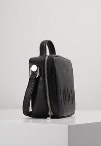 Schwarze Leder-Umhängetasche mit geprägtem "HUGO"-Logo, Seitenreißverschluss und Obergriff. Besitzt eine strukturierte Oberfläche und silberne Hardware-Akzente.