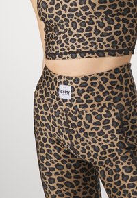 Top i legginsy do aktywności w print w panterkę w odcieniu tan z czarnymi akcentami. Charakteryzują się dopasowanym krojem, widocznymi szwami oraz naszywką z logo na pasie.