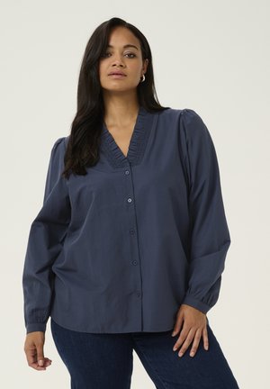 Blouse bleu marine boutonnée avec un décolleté en V, des détails plissés, des manches longues bouffantes et une coupe décontractée. Tissu lisse avec un léger éclat.