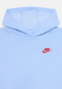 Šviesiai mėlynas džemperis su gobtuvu turi priekinę kišenę, didelį gobtuvą ir raudoną išsiuvinį Nike logotipą kairėje krūtinės pusėje. Minkšta medžiaga su lygiu paviršiumi.