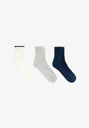 Trois chaussettes montantes côtelées en blanc, gris clair et marine, chacune avec une petite bordure froncée au niveau du bord-côte.