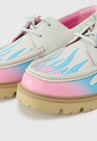 Chaussures en cuir blanc avec motifs de flammes roses et bleues, semelles en caoutchouc beige, lacets blancs et doublure intérieure rose.