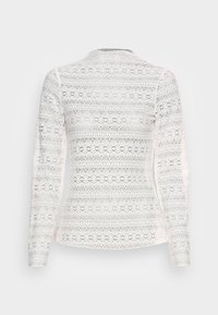 Vit spetsblus med långa ärmar som har intrikata blommönster och en figurnära silhuett, med rund halsringning och en strukturerad yta.