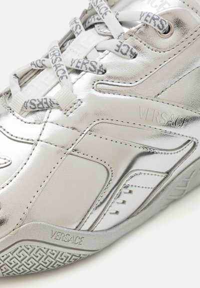 Baskets sportives argentées en cuir métallique. Présentent une surface texturée, un logo bien en vue et des accents à motifs sur les lacets et la semelle.