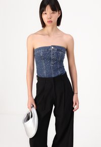 Top bez ramínek z denimu se kamenovými doplňky, modré barvy, přiléhavého střihu, v kombinaci s černými širokými kalhotami a stříbrnou psaníčkovou kabelkou.