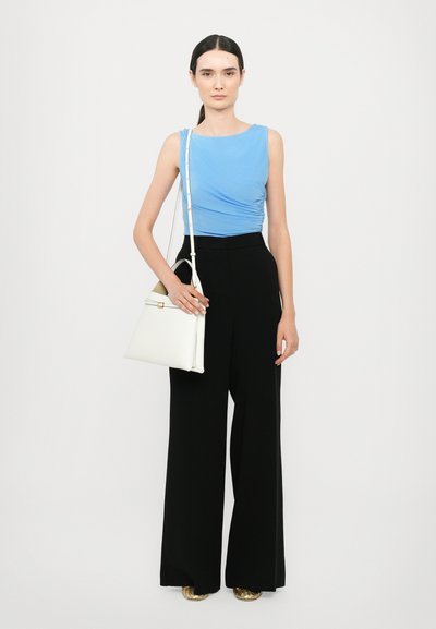 Top sin mangas azul claro, pantalones negros de pierna ancha y un bolso blanco. El conjunto presenta texturas suaves y un diseño elegante.