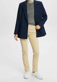 Blazer navy, suéter gris texturizado, pantalones beige ajustados y zapatillas blancas. El blazer tiene cierre de doble botón y corte entallado.