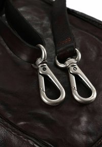 Borsa in pelle marrone con due clip metalliche argento, caratterizzata da una texture liscia e dettagli di cucitura, che mostra una tonalità ricca e scura.