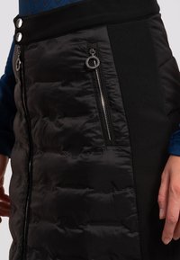 Falda negra acolchada con bolsillos con cremallera, diseño ajustado y paneles de tela en contraste. Incluye dos botones decorativos en la cintura.