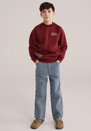 Bordo dukserica s okruglim izrezom i bijelim tekstom; plave i bijele prugaste hlače; smeđe natikače; ležerni kroj.