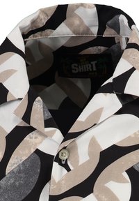 Camisa de manga corta con cuello, que presenta un atrevido patrón abstracto en negro, blanco y beige, y un cierre de botón único.