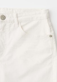 Primo piano dell'area della tasca anteriore di jeans in denim bianco con dettagli in metallo, tra cui bottone e rivetti.