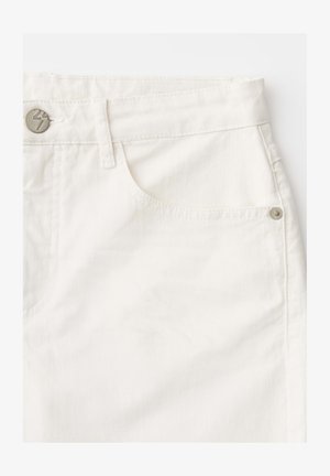 Gros plan sur la zone de la poche avant d'un jean en denim blanc avec des détails de bouton en métal et de rivet.
