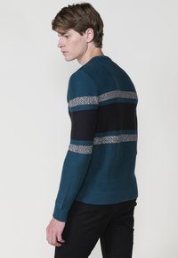 Jersey de punto en verde azulado con rayas horizontales en azul marino oscuro y gris. Puños y dobladillo acanalados. Diseño clásico de cuello redondo.