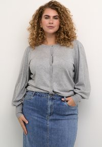 Lichtgrijze gebreide cardigan met knoopsluiting en ballonmouwen, gecombineerd met een blauwe denim kokerrok. Soepele textuur en casual ontwerp.