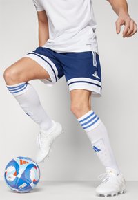 Voetbalkit met blauwe shorts met witte strepen, witte sokken met blauwe strepen, en witte voetbalschoenen. Voetbal met blauw en wit patroon.