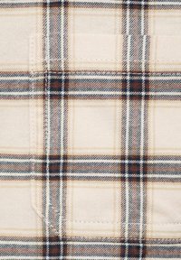 Tessuto della camicia con patta di un leggero beige, caratterizzato da un motivo a quadri nei toni del marrone, blu navy e crema; consistenza morbida con cuciture visibili.