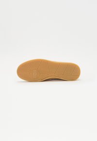 Talpa de sneaker cu o suprafață din cauciuc texturat de tip gumă, având un model în evantai, un logo circular și detalii de design de culoare gri deschis deasupra.