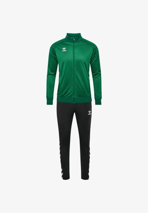 Grøn zip-jacket med høj krave, parret med sorte tapered bukser. Begge har logo-detaljer. Glat tekstur, atletisk pasform.