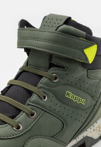 Baskets montantes vertes avec un tissu texturé et un dessus en daim, présentant des accents noirs, des perforations et un logo jaune contrastant.