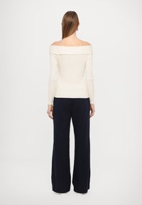 Top creme sem alças com mangas longas, textura canelada, combinado com calças azuis largas. Design simples e minimalista.