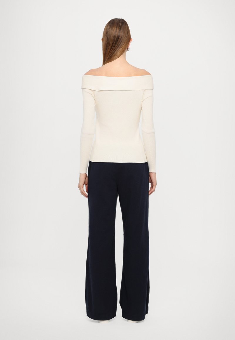Cremefarbene, schulterfreie Bluse mit langen Ärmeln und gerippter Textur, kombiniert mit locker sitzenden marineblauen Hosen. Einfaches, minimalistisches Design.