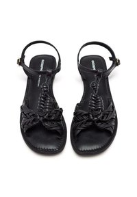 Sandales en cuir noir avec des sangles tressées, une forme de pied carrée et une bride de cheville avec une fermeture à boucle dorée. Design à semelle plate.