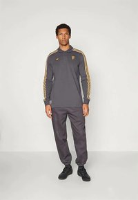 Γκρι πουκάμισο πόλο με μακριά μανίκια και κίτρινες ρίγες, με γιακά και λογότυπο, συνδυασμένο με σκούρες παντελόνες και μαύρα παπούτσια.