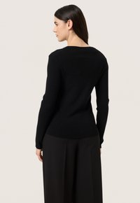 Schwarzer Langarmpullover mit Rundhalsausschnitt und gerippter Textur. Figurbetonte Silhouette aus glattem Stoff, getragen mit schwarzen weiten Hosen.
