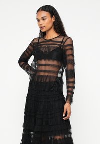 Black lace dress featuring sheer long sleeves, striped texture, ruffled accents, and layered detailing throughout the skirt.