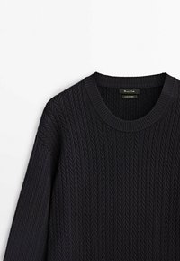 Pull noir en maille torsadée avec encolure ronde, manches longues et col côtelé, présenté sur un fond blanc.