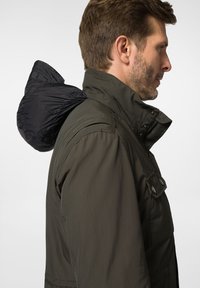 Męska kurtka w ciemnooliwkowym kolorze z wysokim kołnierzem, zatrzaskami, czystą, odpinaną kapturem oraz gładkim, wodoodpornym materiałem.