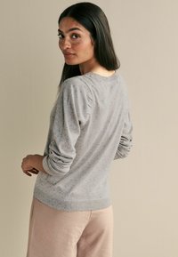Hellgrauer Pullover mit gesprenkelter Textur, langen Ärmeln und gerippten Bündchen. Kombiniert mit weichen, hellen Hosen.