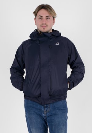 Giacca impermeabile blu navy con cappuccio, chiusura con zip, polsini elasticizzati e un piccolo logo sul petto. Texture liscia, design leggero.