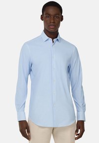 Camisa de manga larga azul claro en un tejido suave y texturizado, con cuello abotonado y tapeta de botones en la parte delantera, con dobladillo curvo.