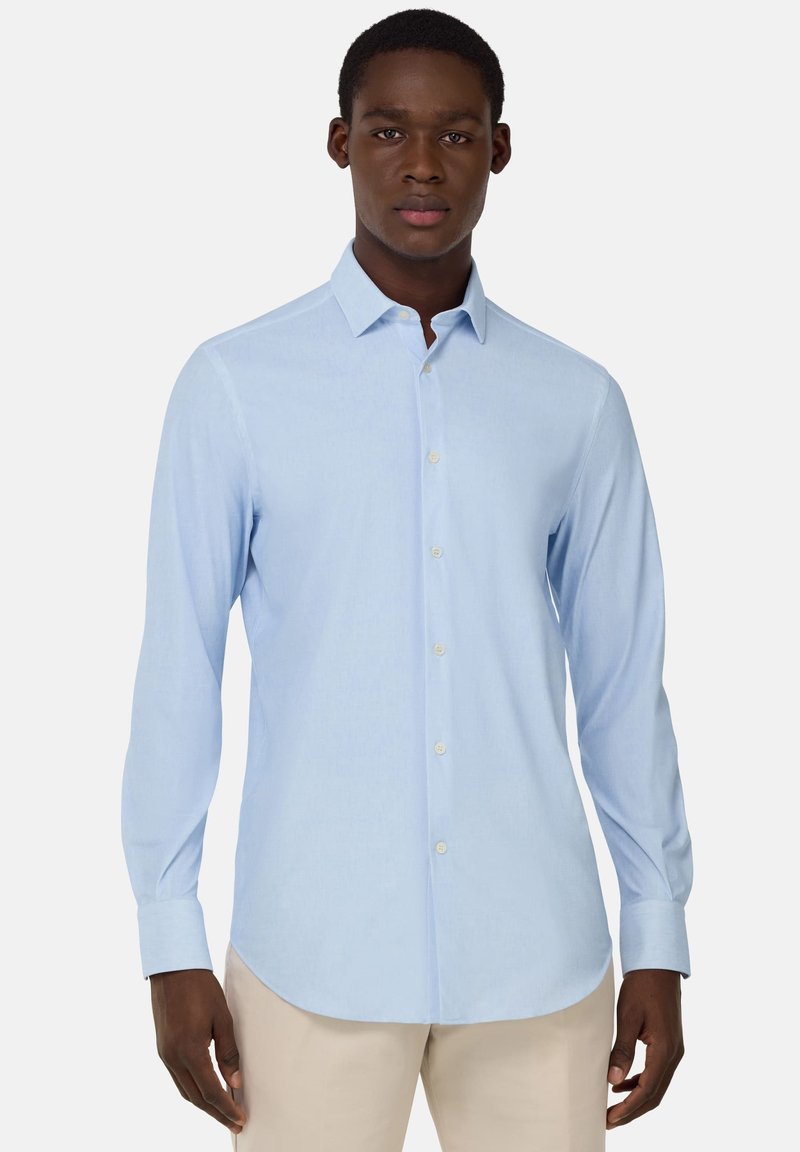 Camisa de manga larga azul claro en un tejido suave y texturizado, con cuello abotonado y tapeta de botones en la parte delantera, con dobladillo curvo.