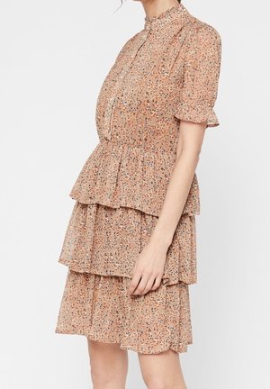 Femme portant une robe à volants à fleurs pêche avec des manches courtes bouffantes et un col montant, sur un fond blanc uni.