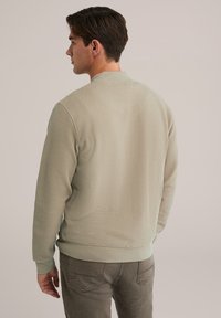 Sudadera de textura verde clara con cuello y puños acanalados, que presenta un diseño informal y un patrón de punto en contraste.