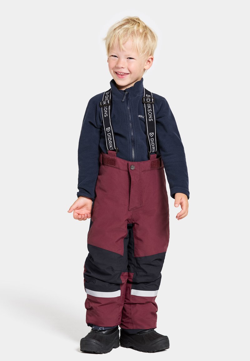 Mörkröda och svarta vinterbyxor med reflexstriper, justerbara hängslen och en figurnära design, kombinerat med en marinblå zip-up fleecetröja.