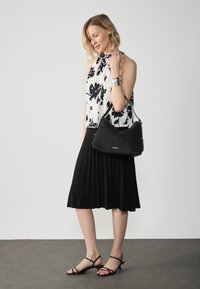 Černá plisovaná sukně, květovaný halter top v bílé a černé barvě, texturovaná černá kabelka a černé sandály s pásky. Stříbrný náramek ve tvaru manžety.