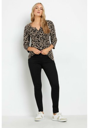 Maglione nero con stampa animale beige, davanti con bottoni, maniche a tre quarti. Abbinato a jeans skinny neri e sneakers bianche.