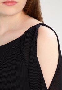 Svart plisserad blus med en axel-design, med en urklippt ärm för en lager-textur och en slät finish.