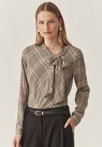 Pikkade varrukatega pluus, millel on ruuduline muster roheliste, punaste ja beežide toonidega. Omab lipsukrae disaini ja sujuvat tekstuuri. Sobitatud musta vöödiga.