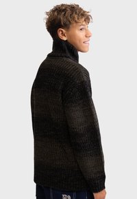 Pull en tricot avec un col montant, motif dégradé vert foncé et noir, matériau texturé et ourlet et poignets côtelés.