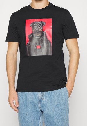 Camiseta negra de algodón con una impresión gráfica de un Rottweiler sobre un fondo rojo, con una etiqueta "HUGO" en un recuadro rectangular.