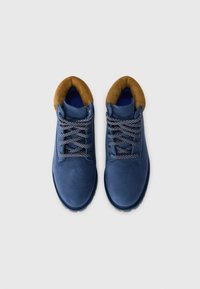 Une paire de bottes bleues à lacets avec des cols rembourrés marron, vues de dessus sur un fond gris uni.