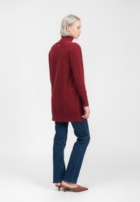 Bordeaux farvet turtleneck sweater med lange ærmer, sidespalter og en lille detalje bagpå, parret med blå jeans og brune hælede mules.