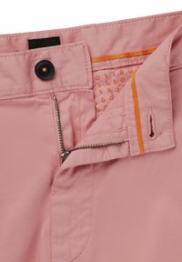 Tela rosa claro con textura suave; presenta un botón negro, una cremallera de metal y costuras de acento naranjas en la cintura y el bolsillo.